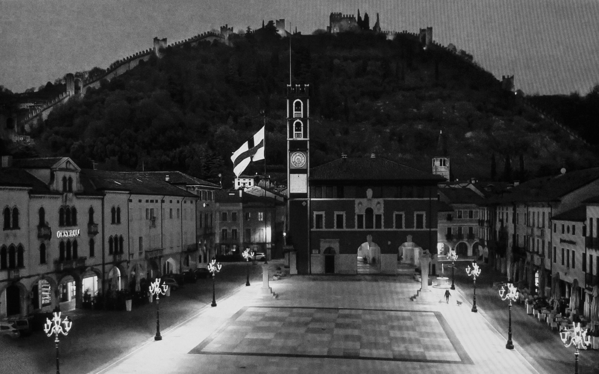 Marostica, Chess Square - The local citizen with two dogs takes an evening stroll through the Scacchi square named by a giant chess set. In the background Castle of Marostica. Province Vicenza, March 26. 2020.